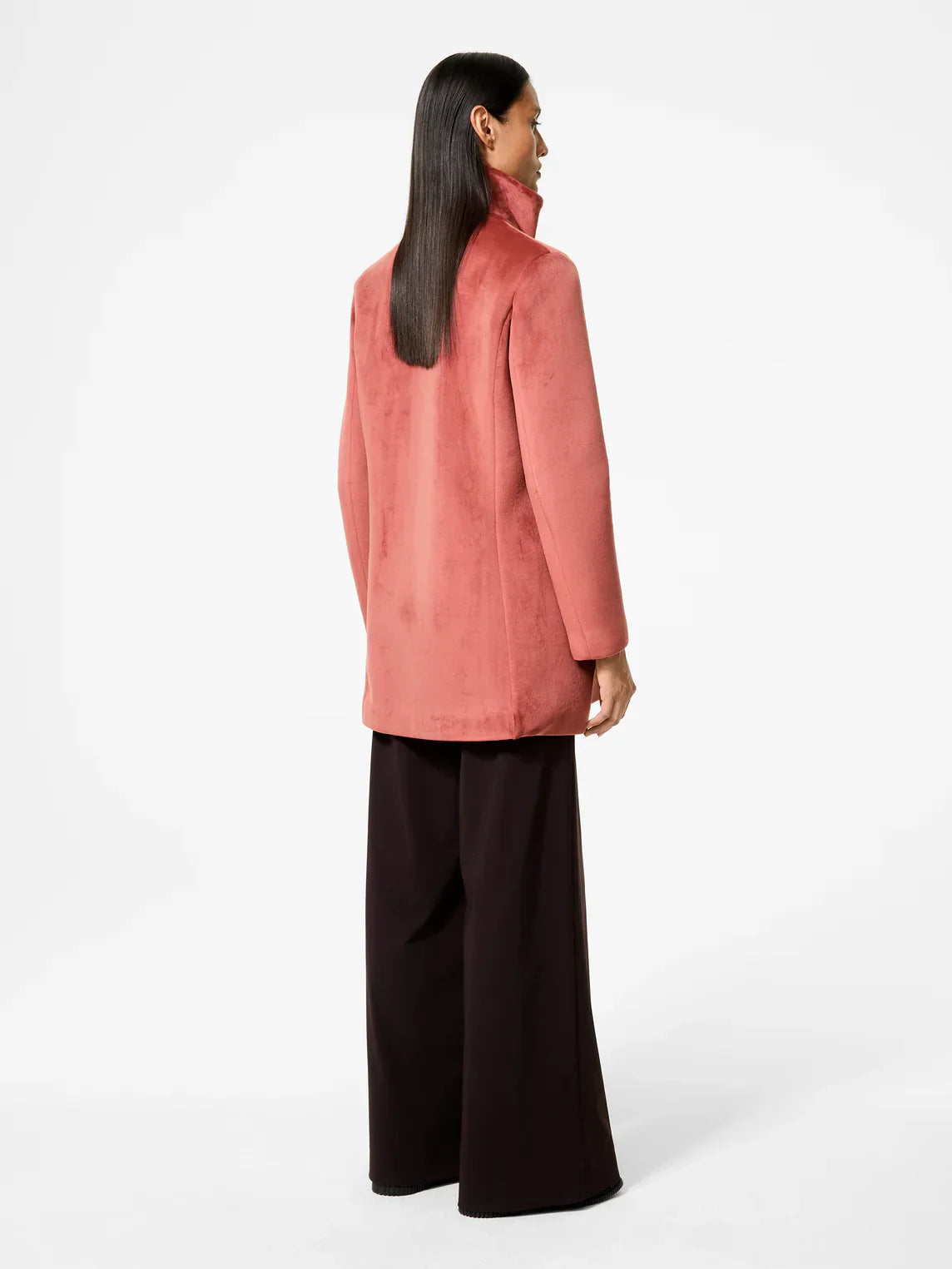 Donna di spalle con giacca rosa in suede e pantaloni larghi neri, moda elegante donna.