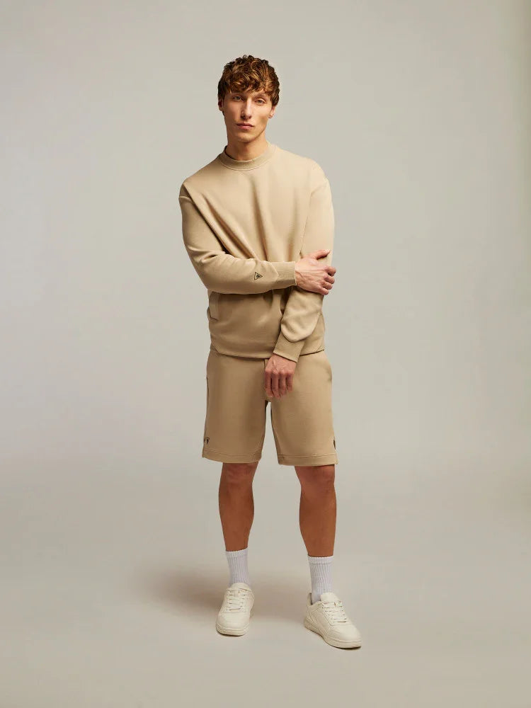 Modello uomo con felpa e bermuda beige, calzini bianchi e sneakers, abbigliamento casual.