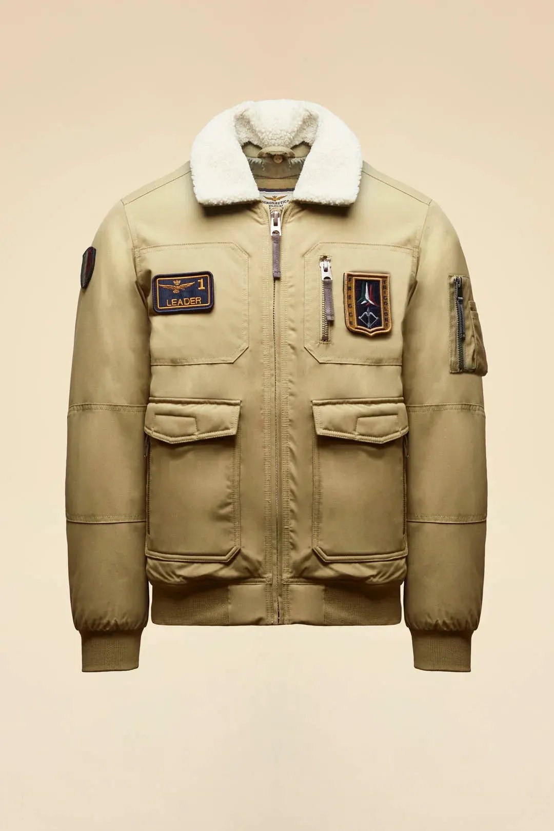 Giubbotto bomber beige da uomo con colletto in pelliccia e patch decorative stile aviatore.