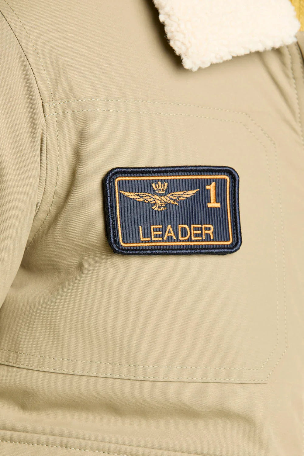 Dettaglio giubbotto beige con colletto in pile e patch ricamata LEADER sulla spalla