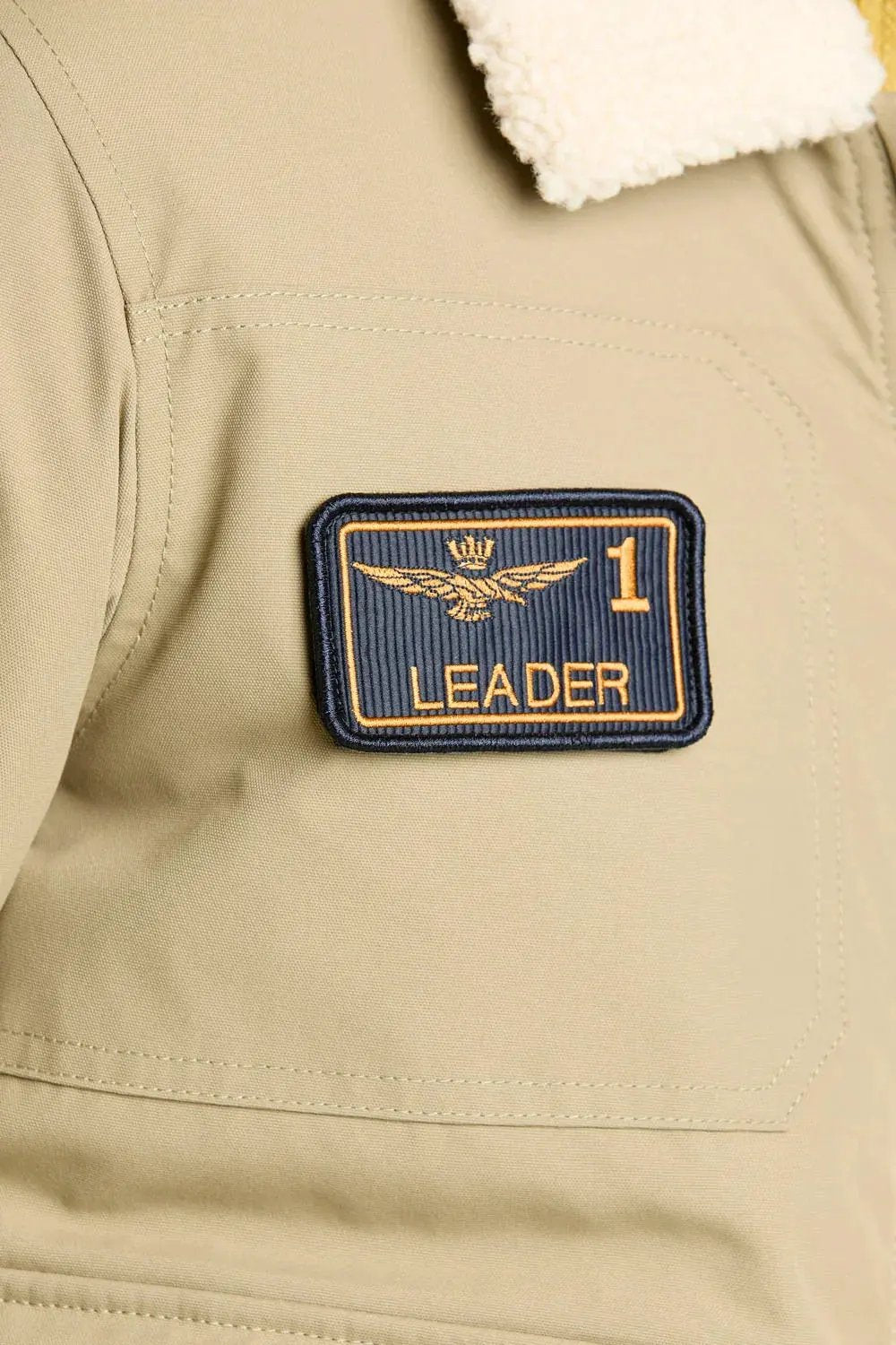 Dettaglio giubbotto beige con colletto in pile e patch ricamata LEADER sulla spalla