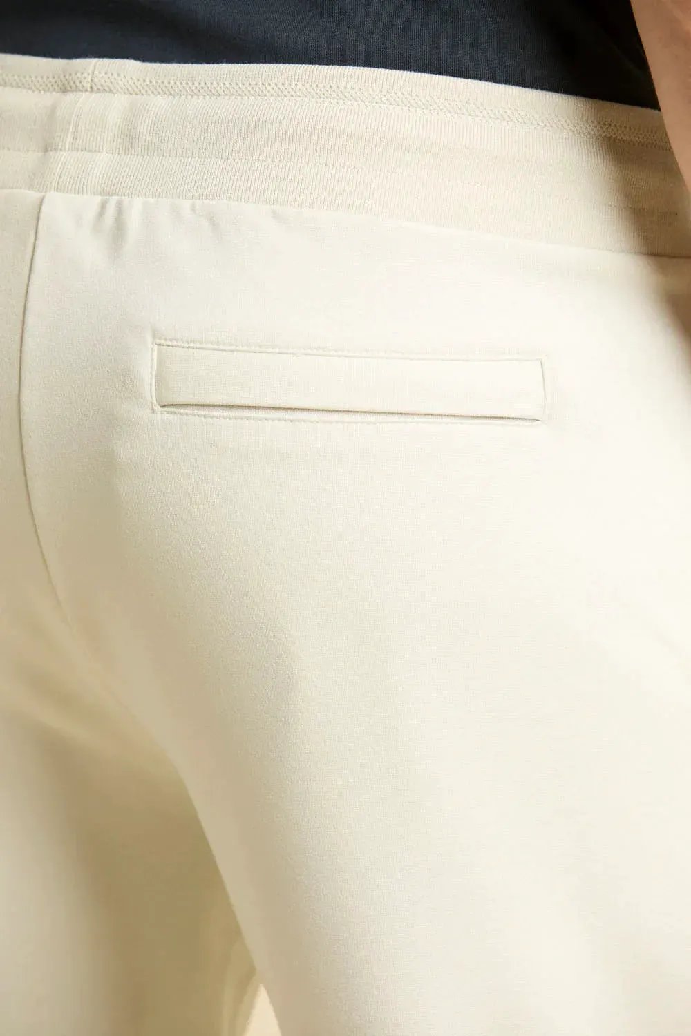 Dettaglio tasca posteriore su pantalone sportivo uomo color ghiaccio in cotone.
