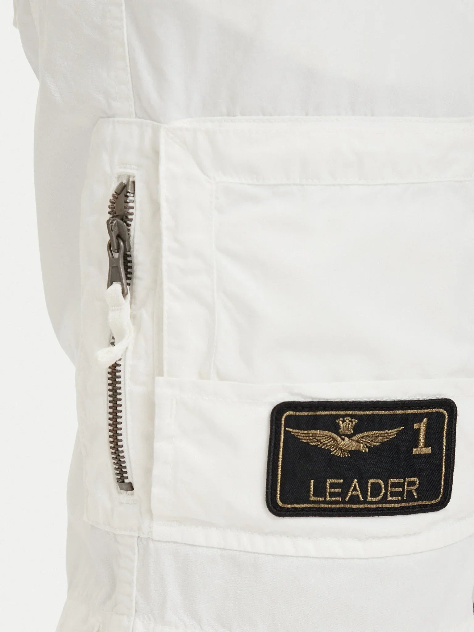 Dettaglio pantaloncini bianchi da uomo con tasca laterale, zip e patch "Leader 1" ricamata.