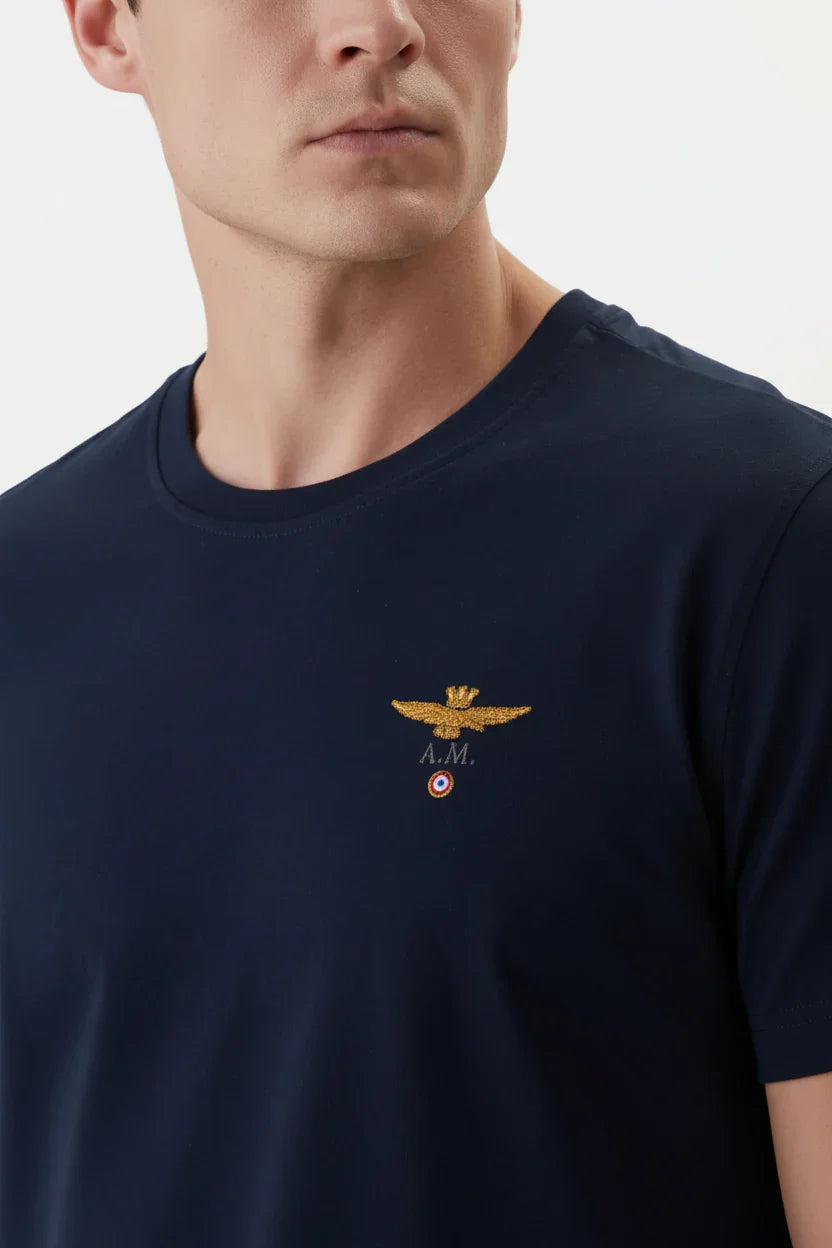 Uomo con t-shirt blu scuro regular fit, logo dorato ricamato sul petto, stile casual.