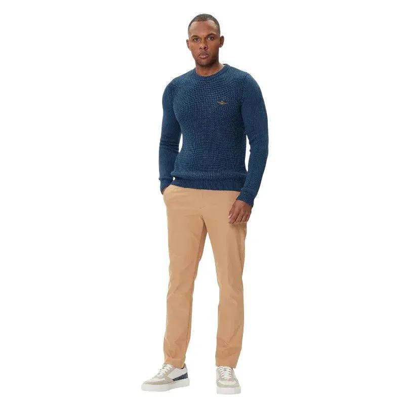 Uomo con maglione girocollo in lana blu, pantaloni beige e sneakers, moda abbigliamento maschile.