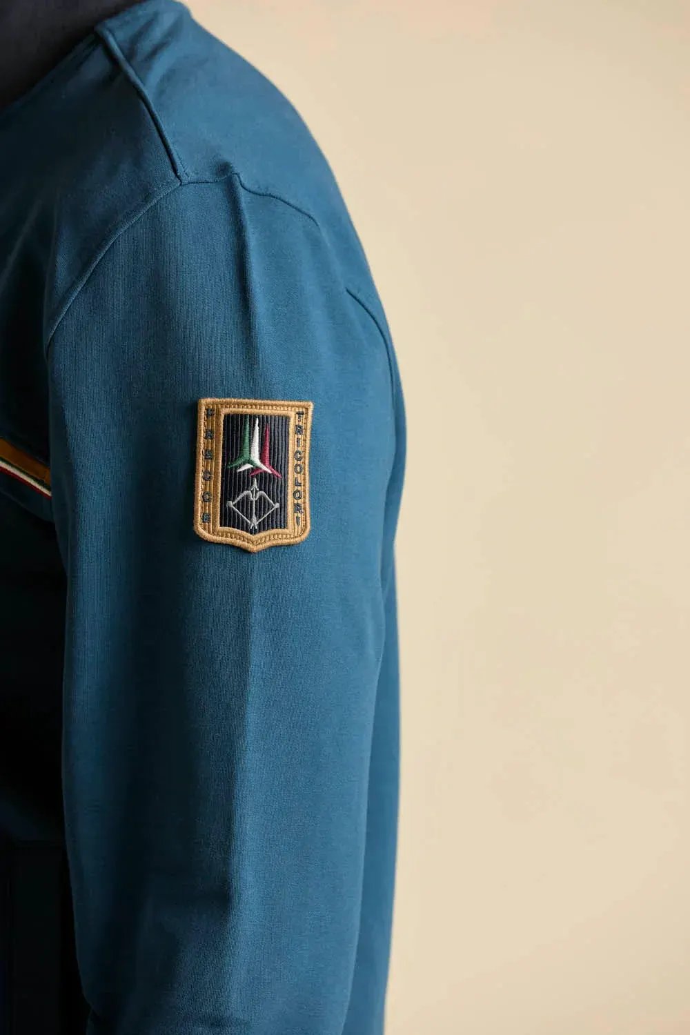 Felpa blu uomo con zip, dettagli tricolore e patch ricamata sulla manica sinistra.