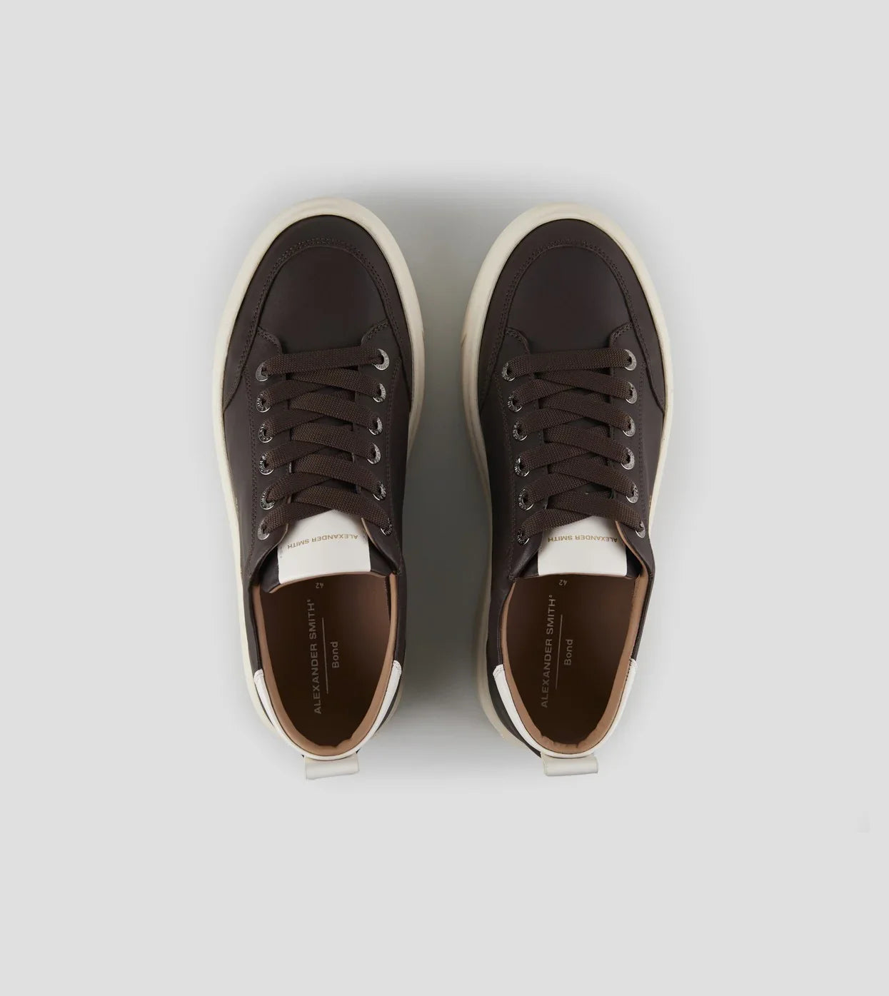 Sneakers uomo marroni con suola bianca, design moderno, lacci scuri, vista dall'alto.
