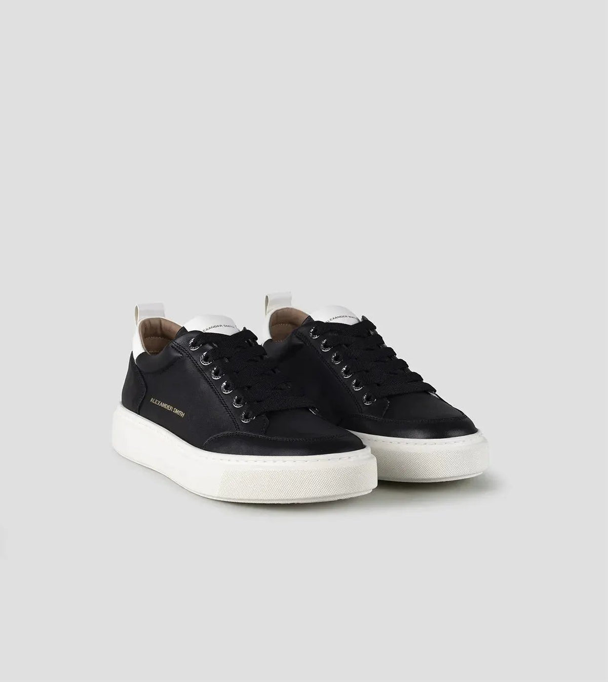 Sneakers uomo nere con suola bianca, dettagli logo dorato e tallone bianco, stile casual elegante.