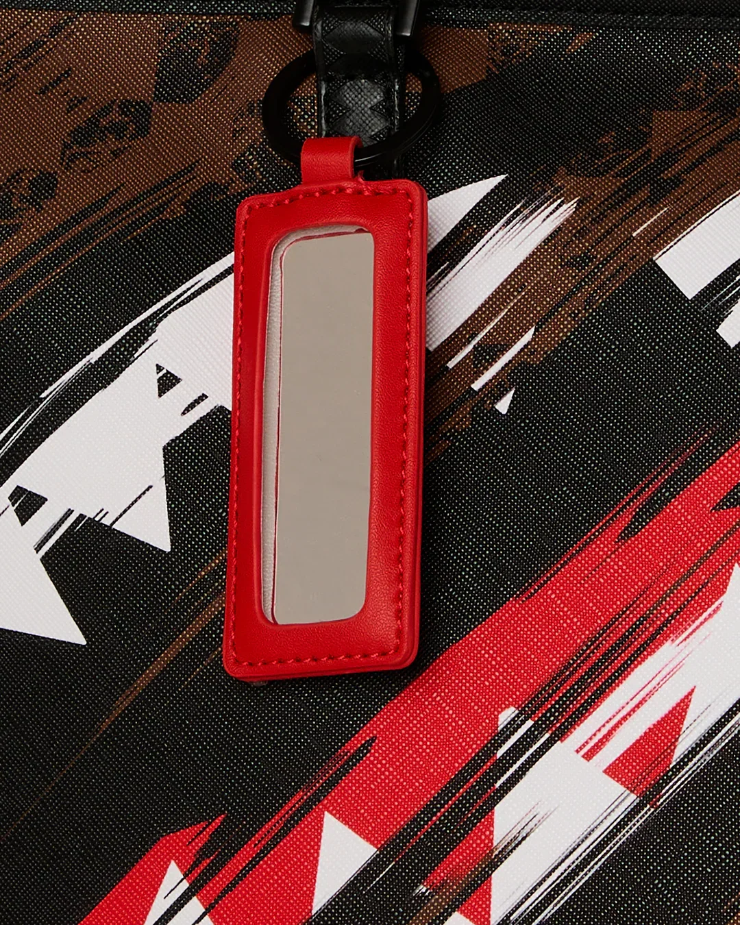 Porta etichetta in pelle rossa su borsa fantasia astratta nera, marrone e rossa