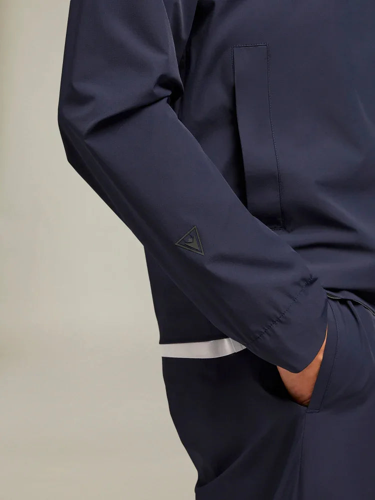 Dettaglio giacca uomo blu scuro elegante, tessuto tecnico con tasca laterale e logo discreto sulla manica.