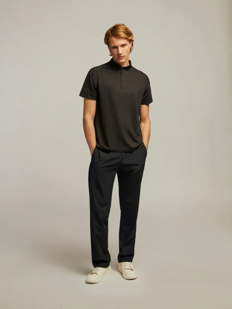 Uomo indossa polo nera a maniche corte, pantaloni scuri eleganti e sneakers bianche