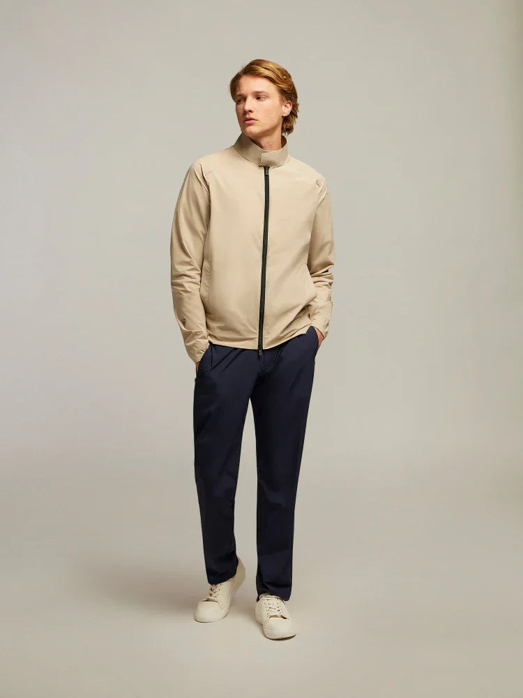 Uomo con giacca beige zip, pantaloni blu e sneakers bianche su sfondo neutro, moda uomo elegante