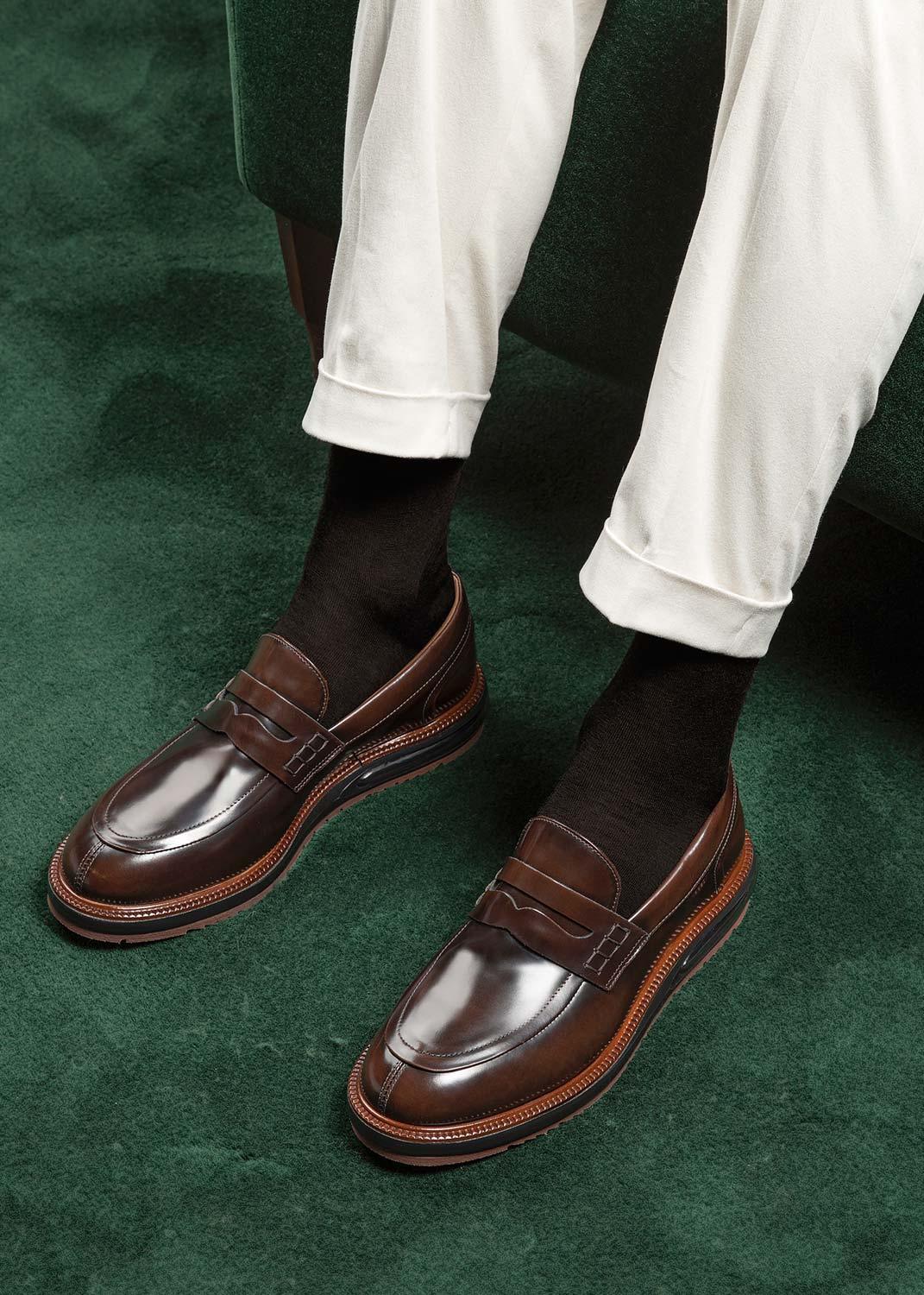 Mocassini uomo in pelle marrone lucida, stile elegante, su tappeto verde.