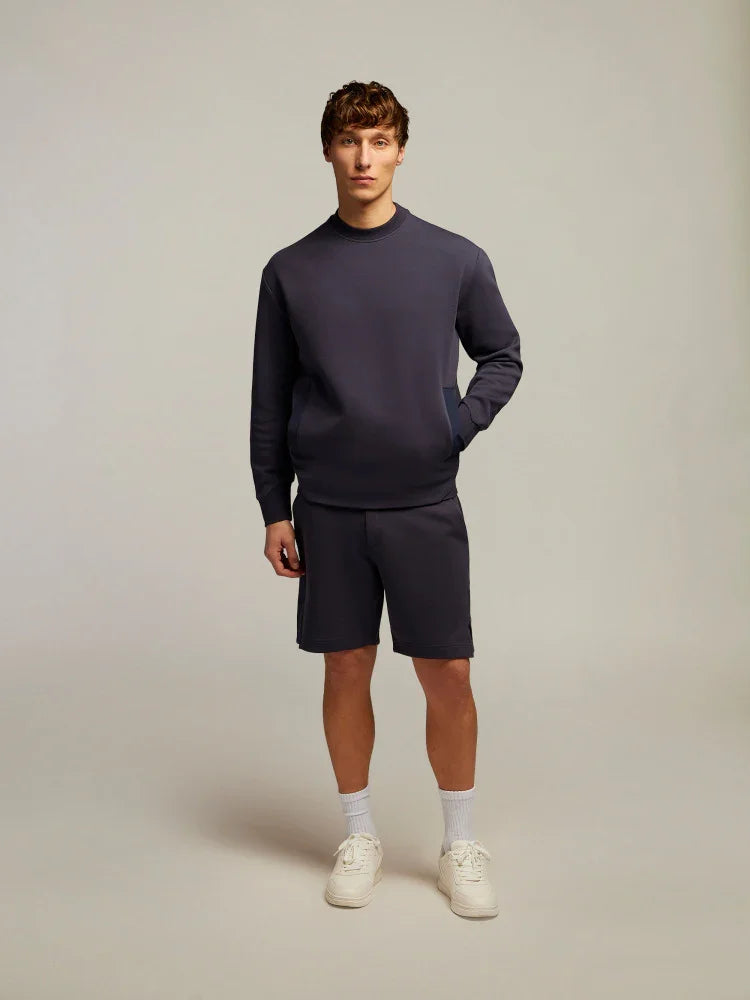 Modello uomo con completo felpa e bermuda blu navy, sneakers bianche, moda casual elegante