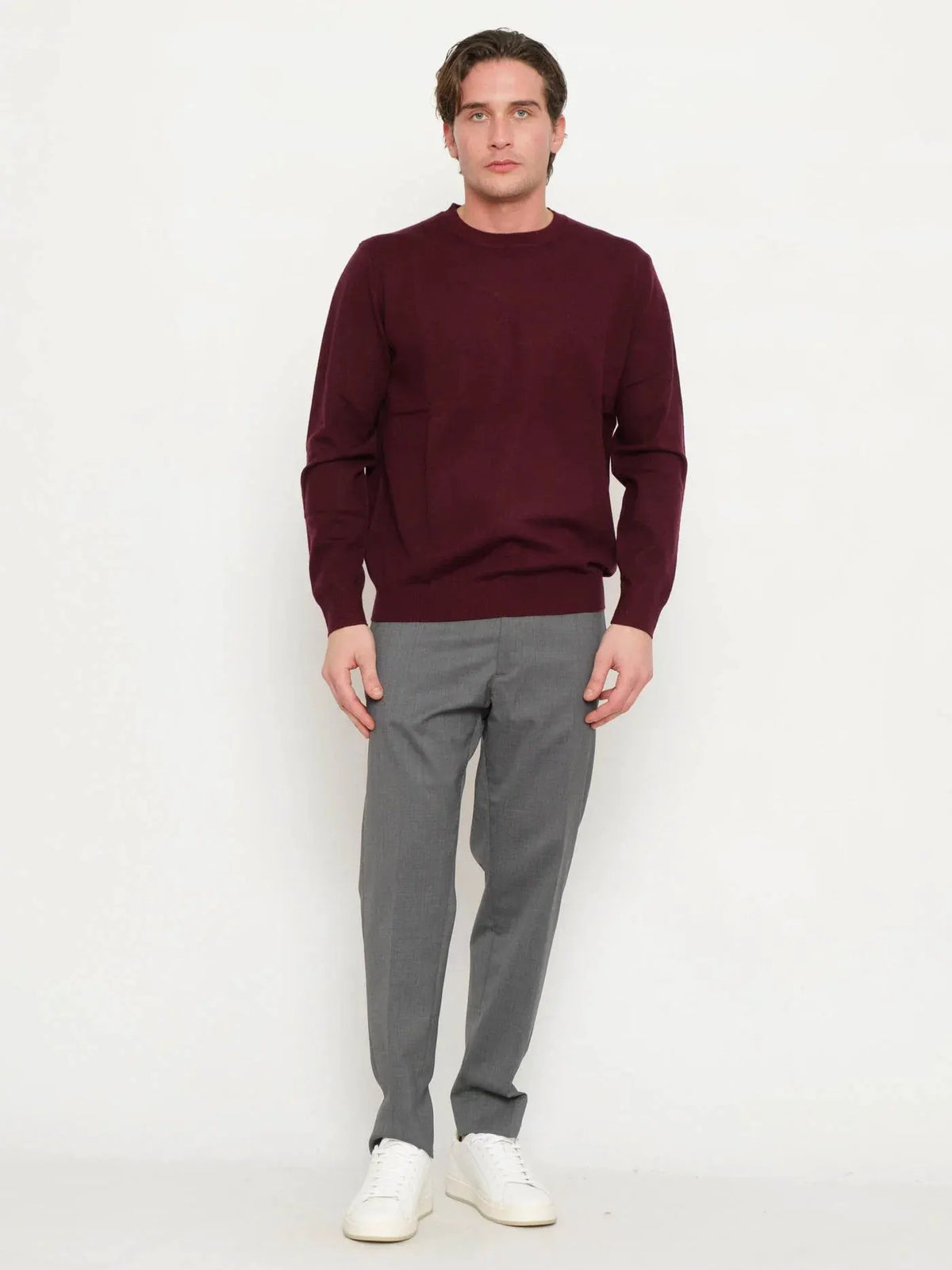 Maglione uomo prugna a girocollo, abbinato a pantaloni grigi eleganti e sneakers bianche.