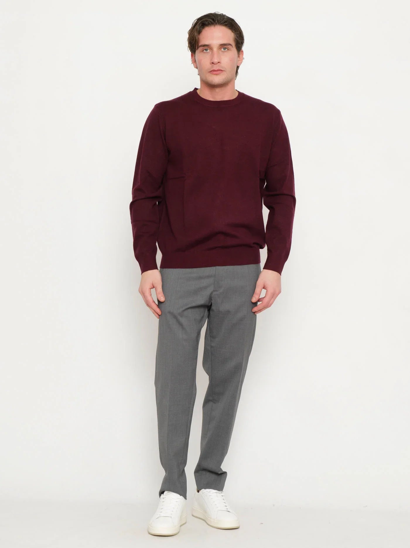 Maglione uomo prugna a girocollo, abbinato a pantaloni grigi eleganti e sneakers bianche.