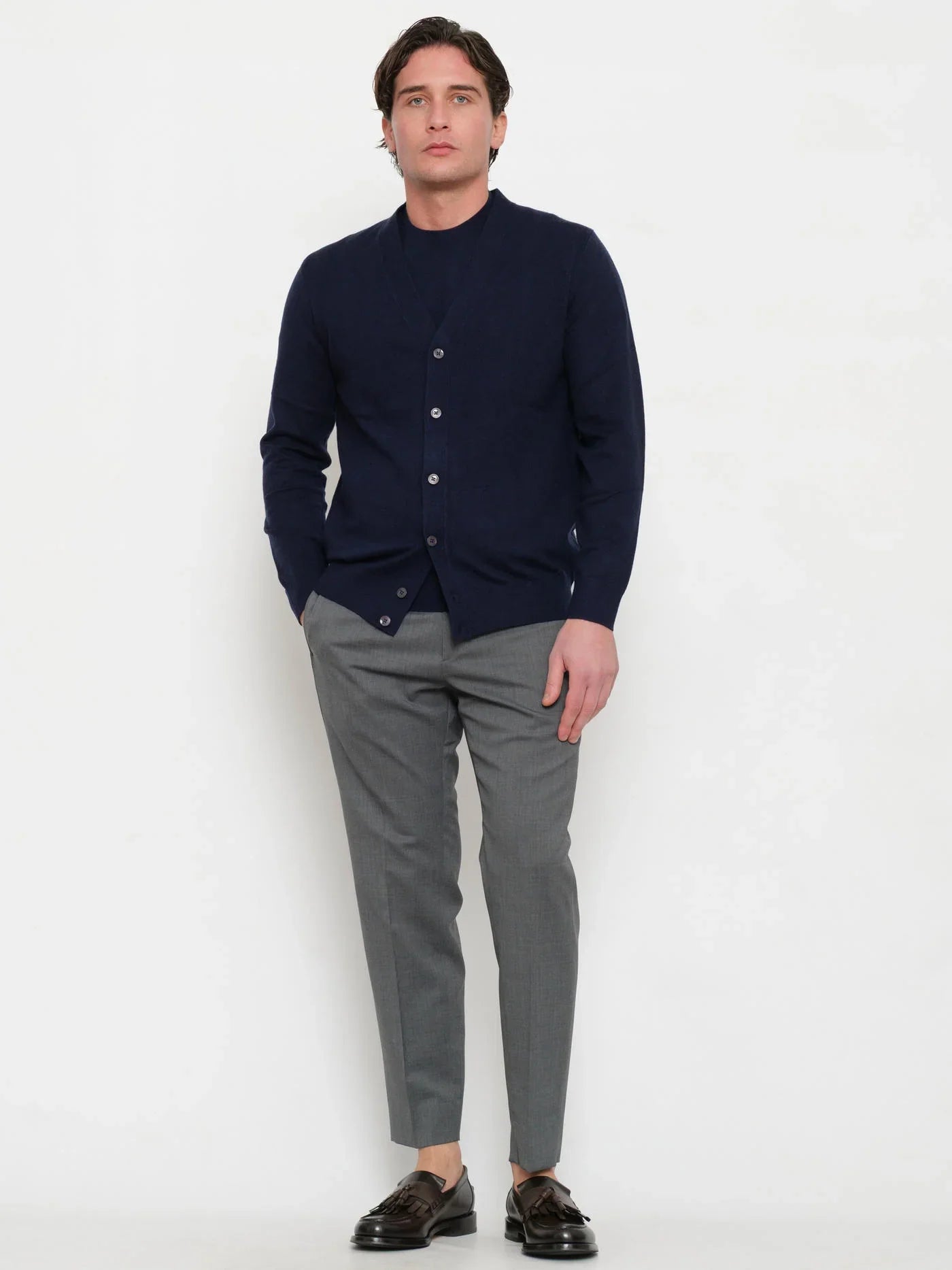 Uomo con cardigan blu notte elegante, pantaloni grigi e mocassini marroni su sfondo bianco