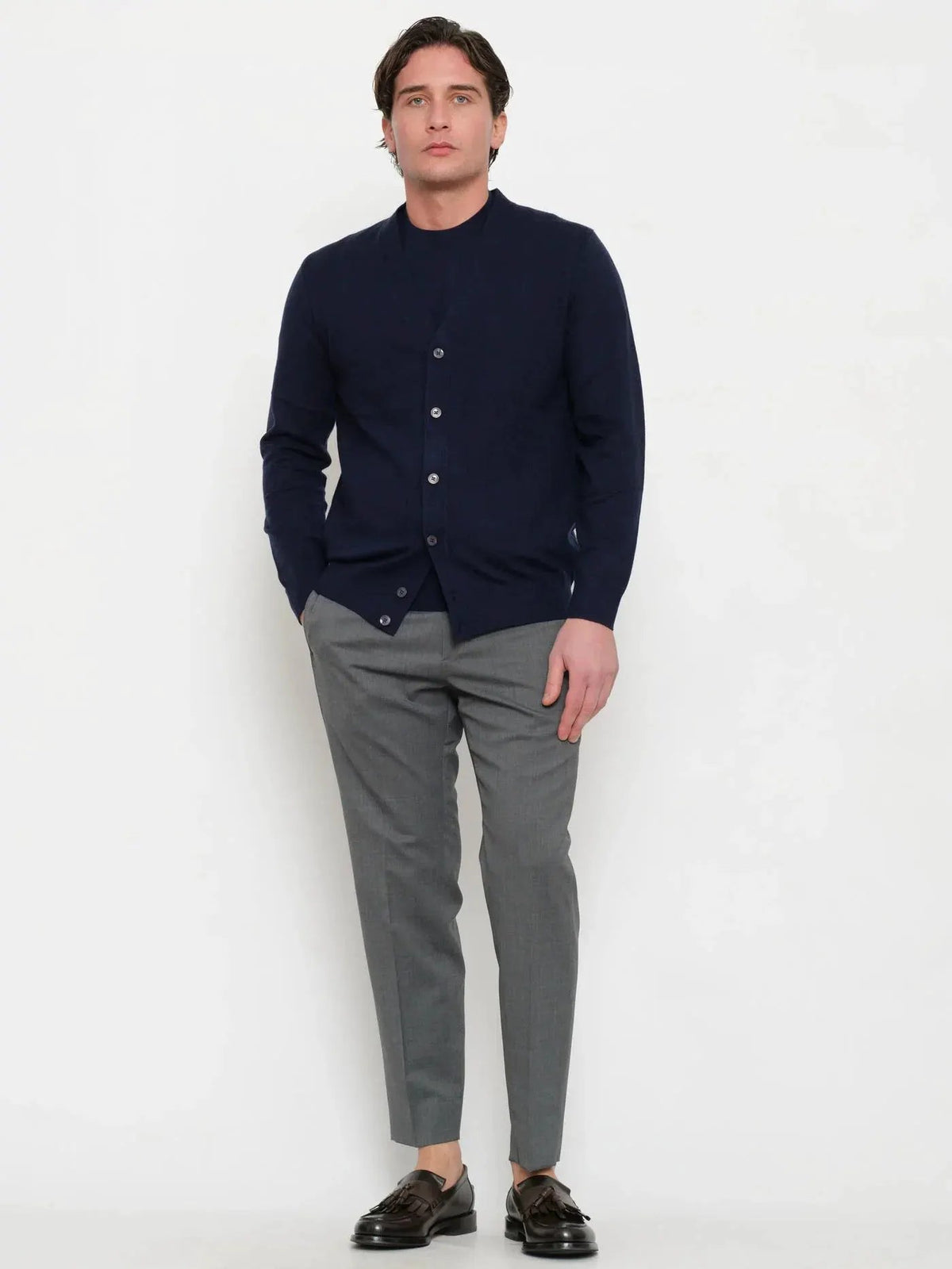Uomo con cardigan blu notte elegante, pantaloni grigi e mocassini marroni su sfondo bianco