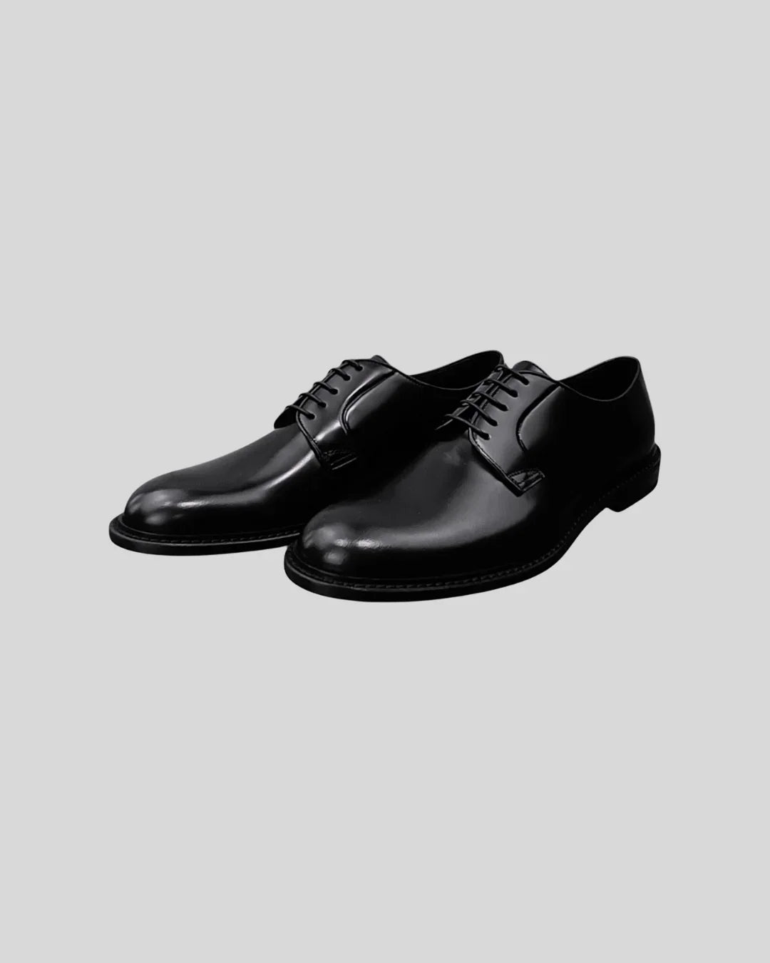 Scarpe Derby uomo in pelle nera lucida con stringhe, eleganti e classiche su sfondo neutro.