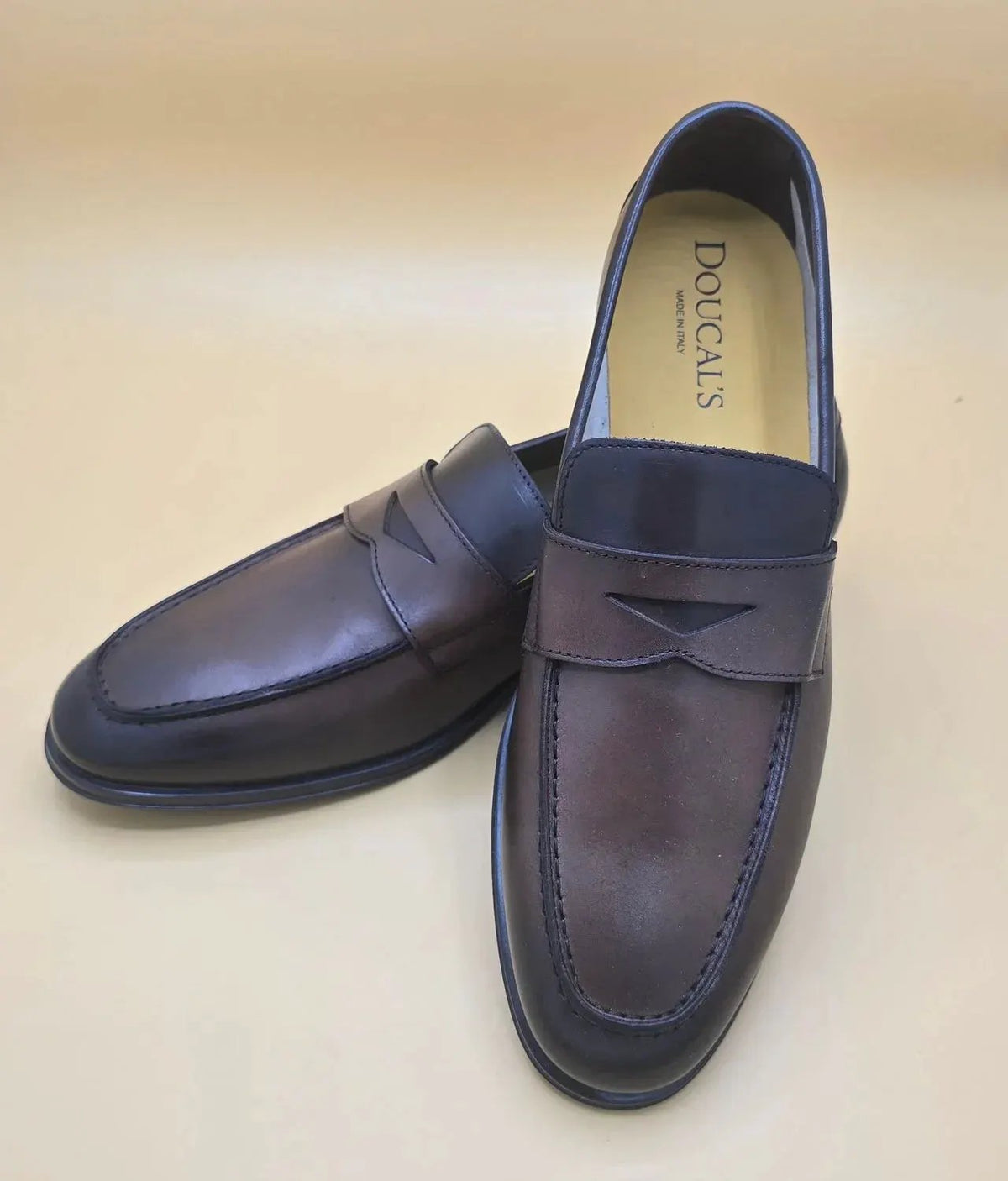 Mocassini uomo in pelle marrone scuro penny loafer eleganti su sfondo beige