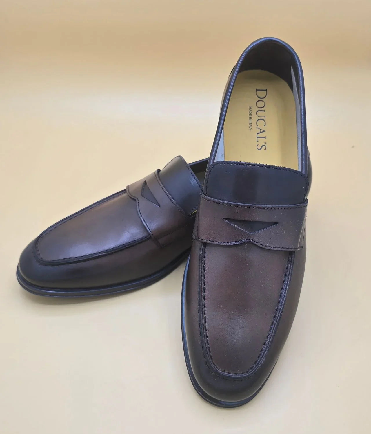 Mocassini uomo in pelle marrone scuro penny loafer eleganti su sfondo beige