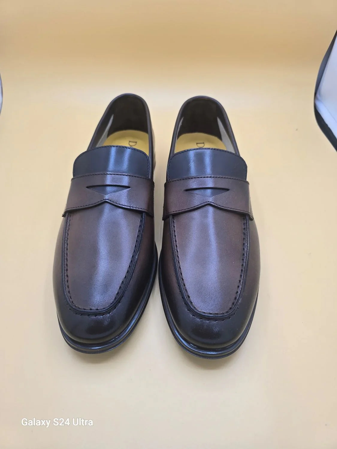 Mocassini penny loafer uomo in pelle marrone scuro, stile elegante su sfondo neutro.