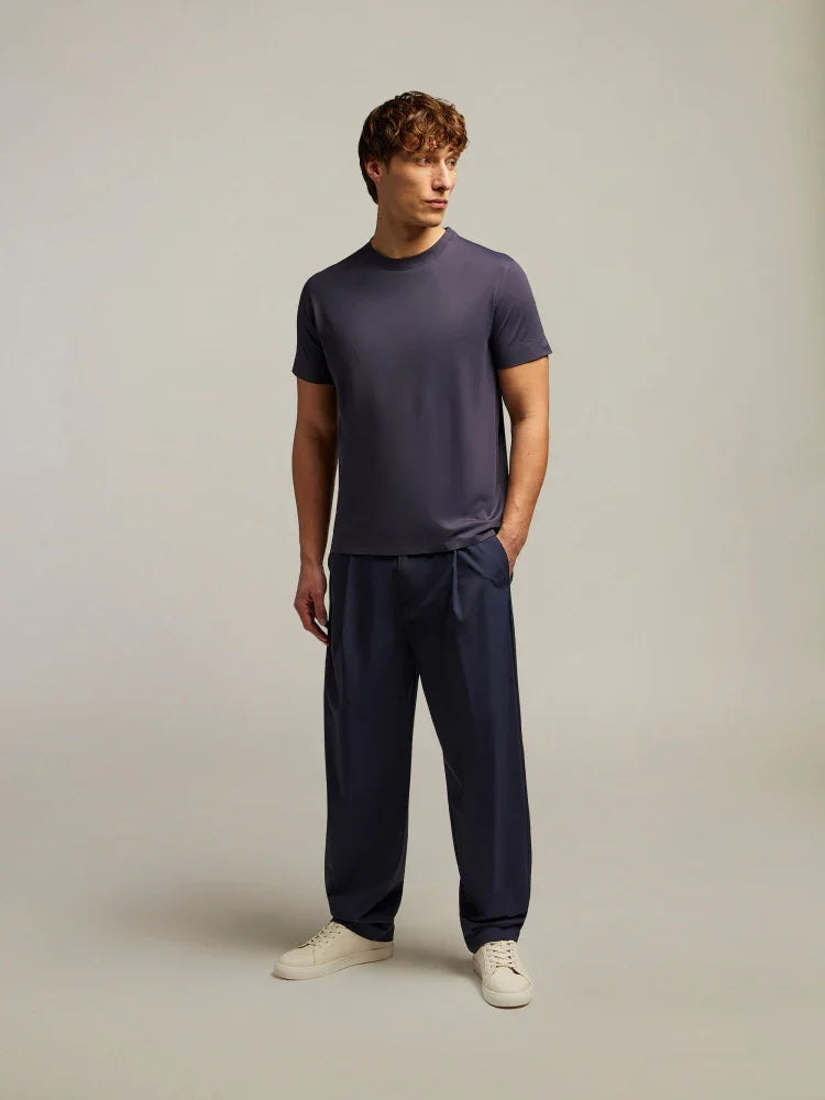 Modello uomo con t-shirt blu scuro, pantaloni eleganti e sneakers in uno studio minimal