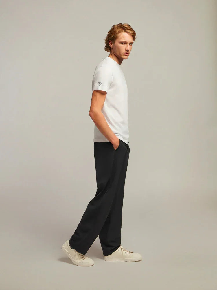 Modello uomo con t-shirt bianca, pantaloni neri e sneakers beige su sfondo neutro.