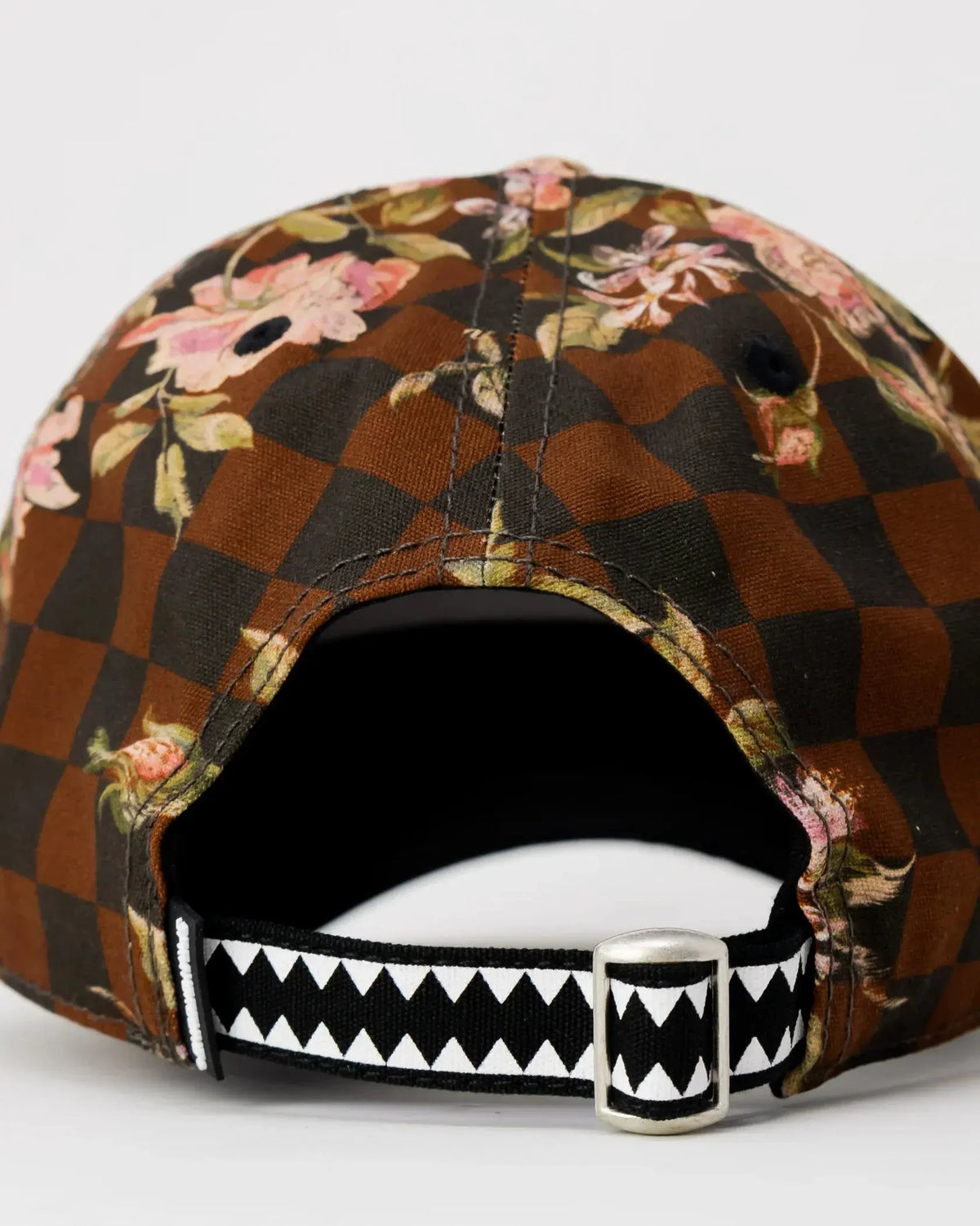 Cappellino con motivo a scacchi marrone e nero, dettagli floreali e cinturino regolabile a zigzag.