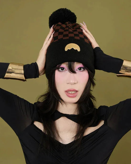 Donna con cappello invernale nero e marrone a scacchi, pompon e dettaglio decorativo dorato, abbigliamento moda donna