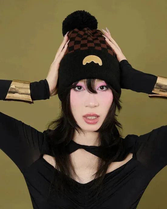 Donna con cappello invernale nero e marrone a scacchi, pompon e dettaglio decorativo dorato, abbigliamento moda donna