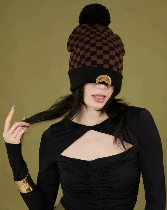 Donna con cappello invernale a scacchi marrone e nero, maglia nera elegante, sfondo verde.
