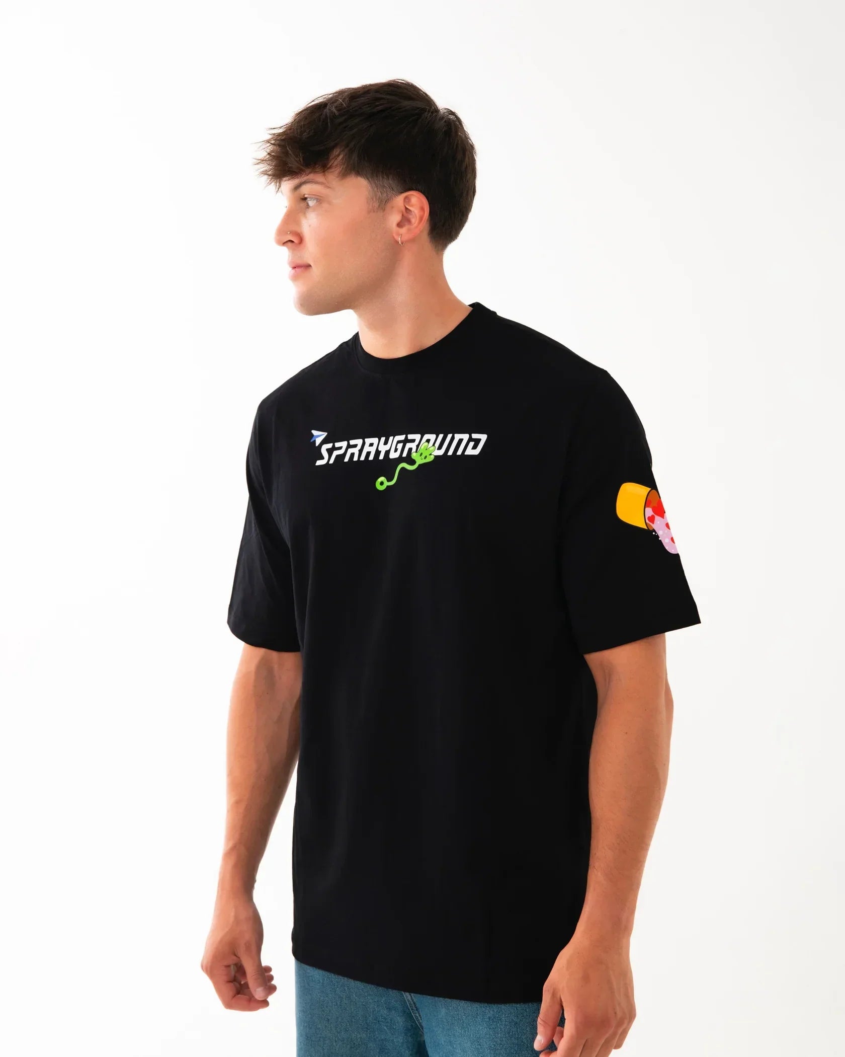 Uomo con t-shirt nera Sprayground, stampa colorata sul petto e sulla manica, jeans blu