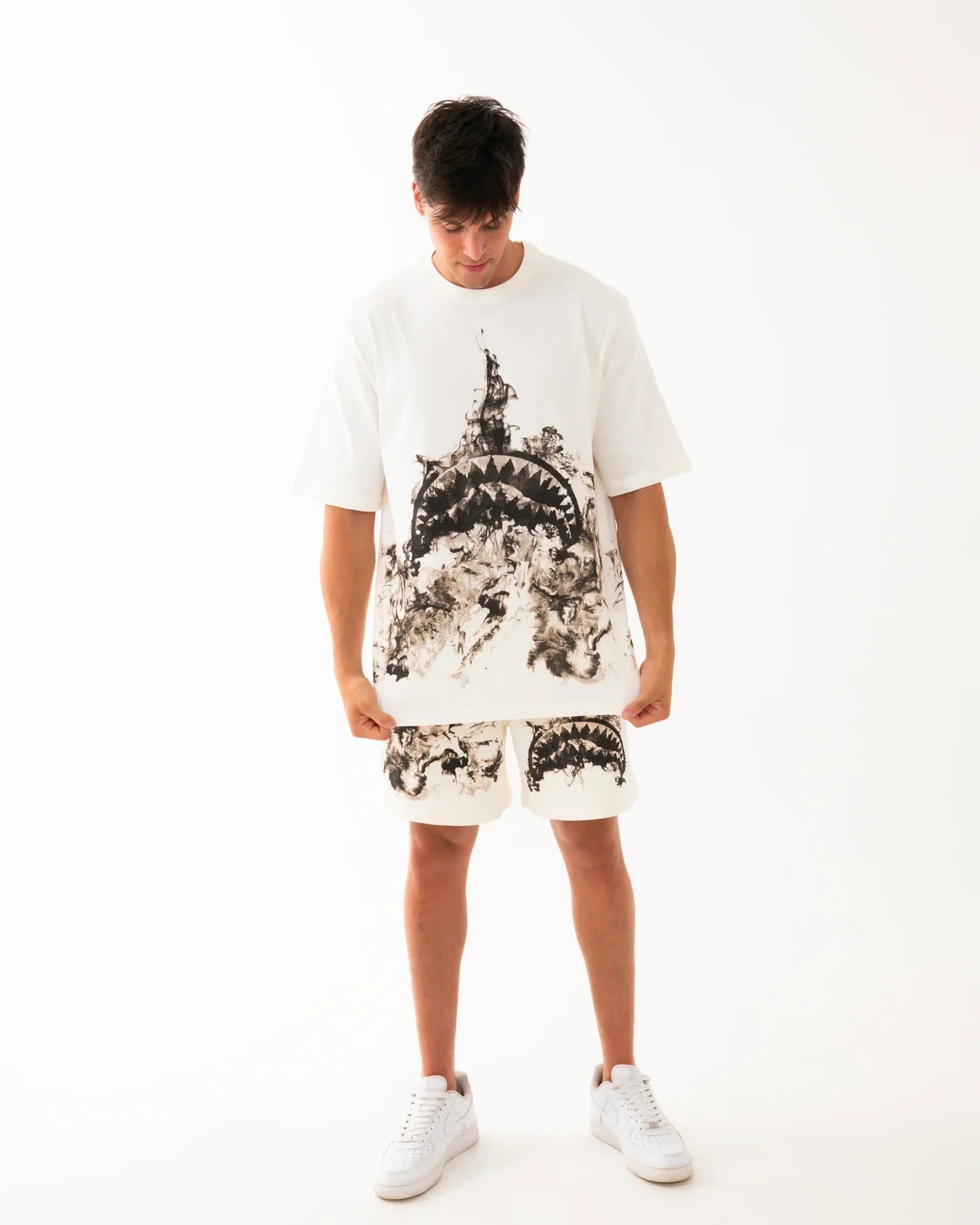 Modello indossa t-shirt e shorts bianchi uomo con stampa grafica nera, sneakers bianche