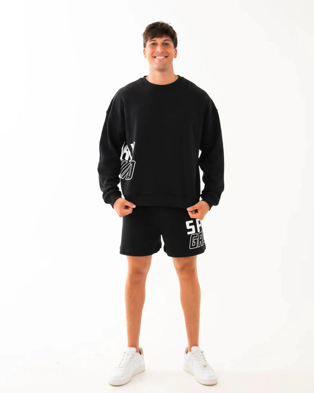 Modello con felpa e shorts neri da uomo, look casual sporty, scarpe bianche, sfondo bianco