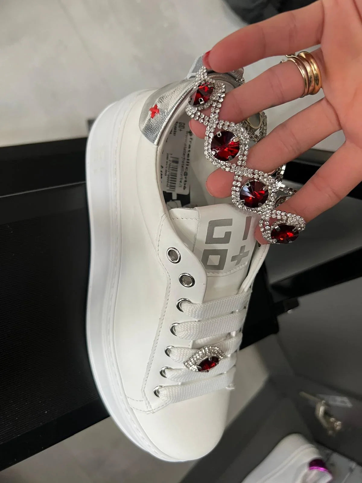 Sneaker bianca con dettagli argento e decorazione gioiello rosso su lacci, stile moda donna