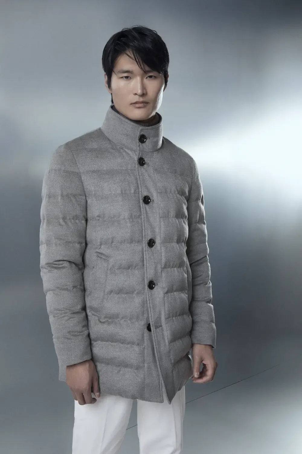 Uomo con piumino grigio melange in lana, stile elegante e contemporaneo, su sfondo neutro.