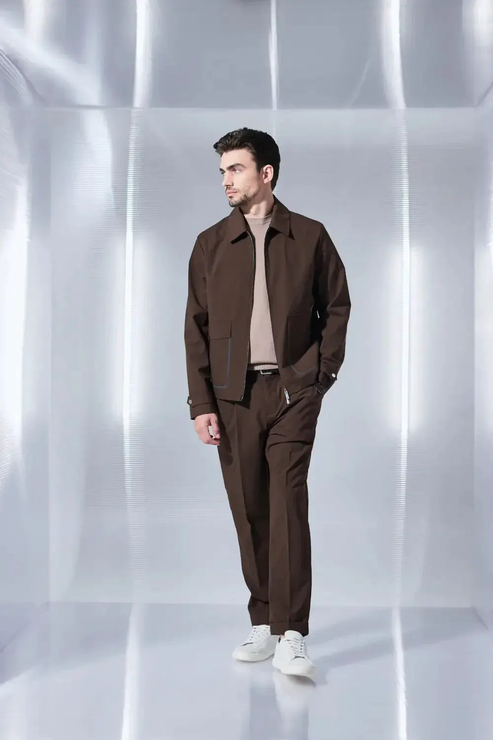 Modello uomo indossa completo marrone primaverile con giacca e pantaloni eleganti, sneakers bianche.