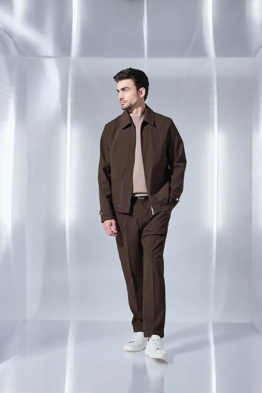 Modello uomo indossa completo marrone primaverile con giacca e pantaloni eleganti, sneakers bianche.