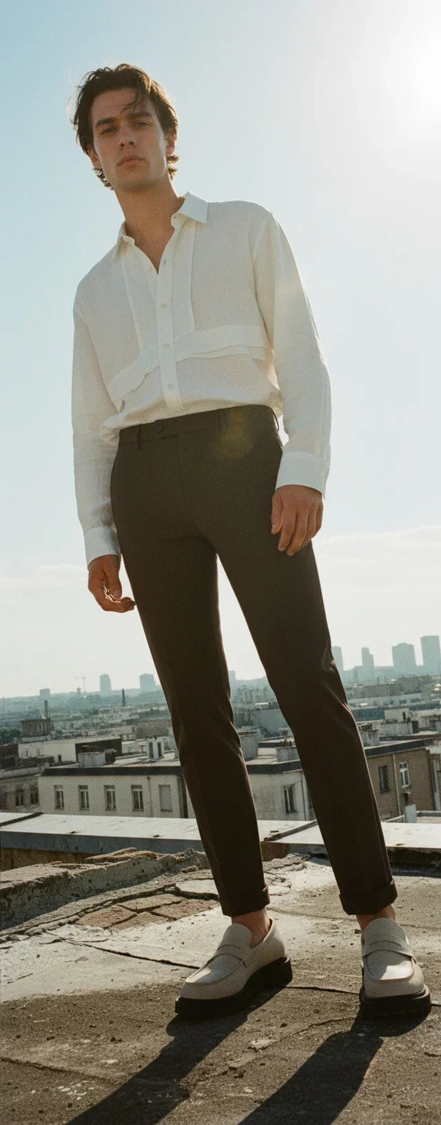 Modello indossa pantalone uomo tecnico stretch marrone con camicia bianca su terrazza urbana