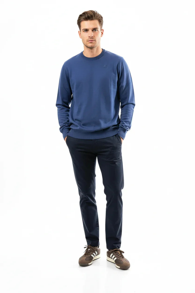 Modello uomo con maglione blu, pantaloni scuri e sneakers marroni su sfondo bianco