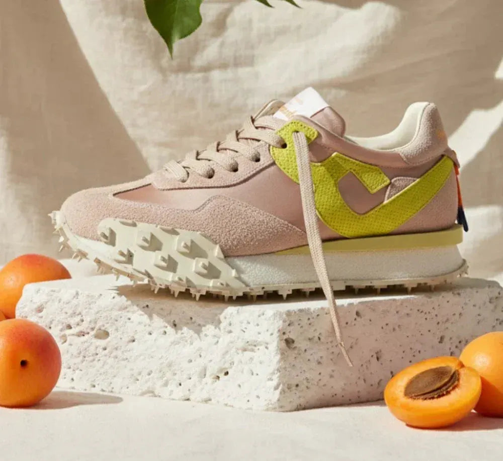 Sneaker da donna beige con dettagli giallo lime su pietra bianca, albicocche intorno.