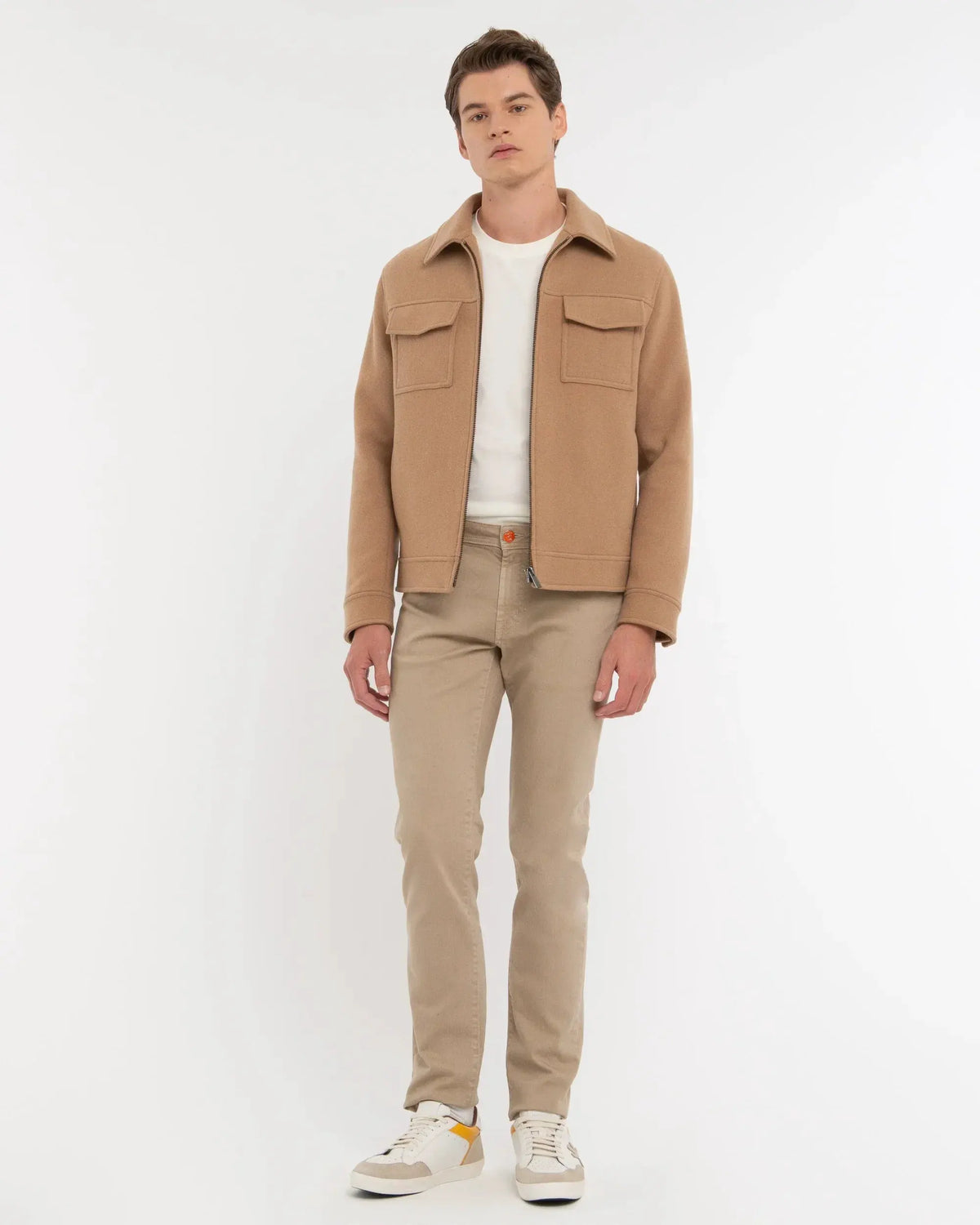 Giacca cammello da uomo con tasche frontali, pantaloni beige e sneakers, stile casual elegante.