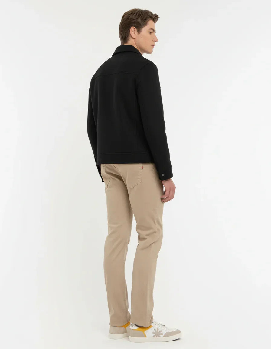 Giacca nera uomo abbinata a pantaloni beige e sneakers bianche, moda casual elegante.
