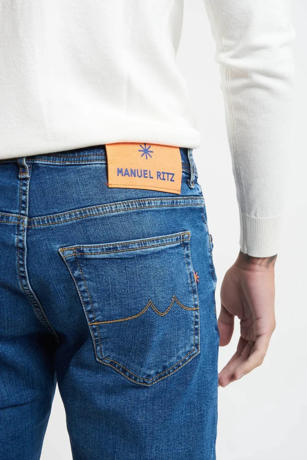 Jeans uomo denim chiaro con patch arancione, dettaglio tasca posteriore e cuciture a vista.