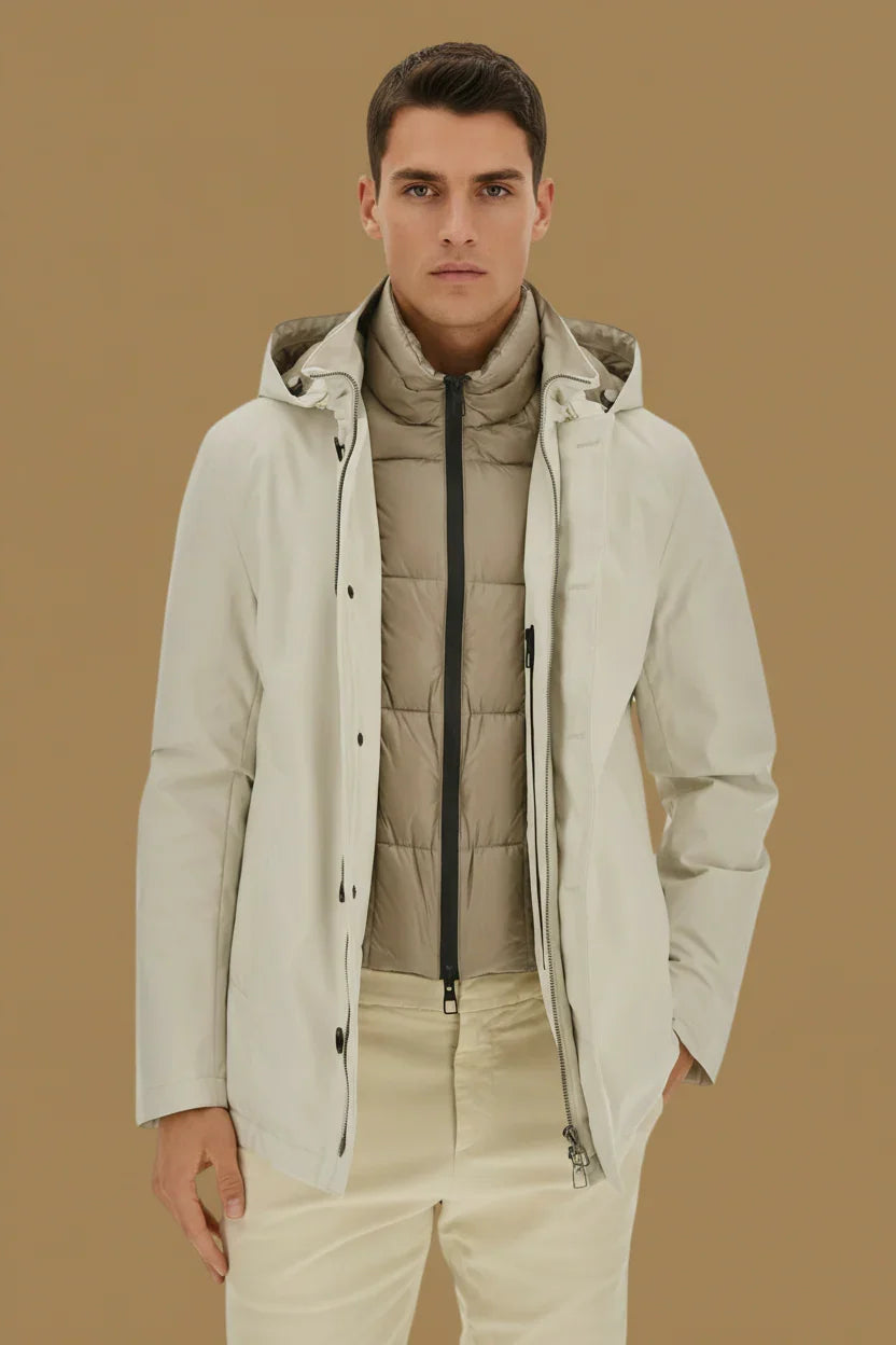 Modello uomo con trench avorio, giacca imbottita beige e pantaloni chiari, moda uomo elegante.