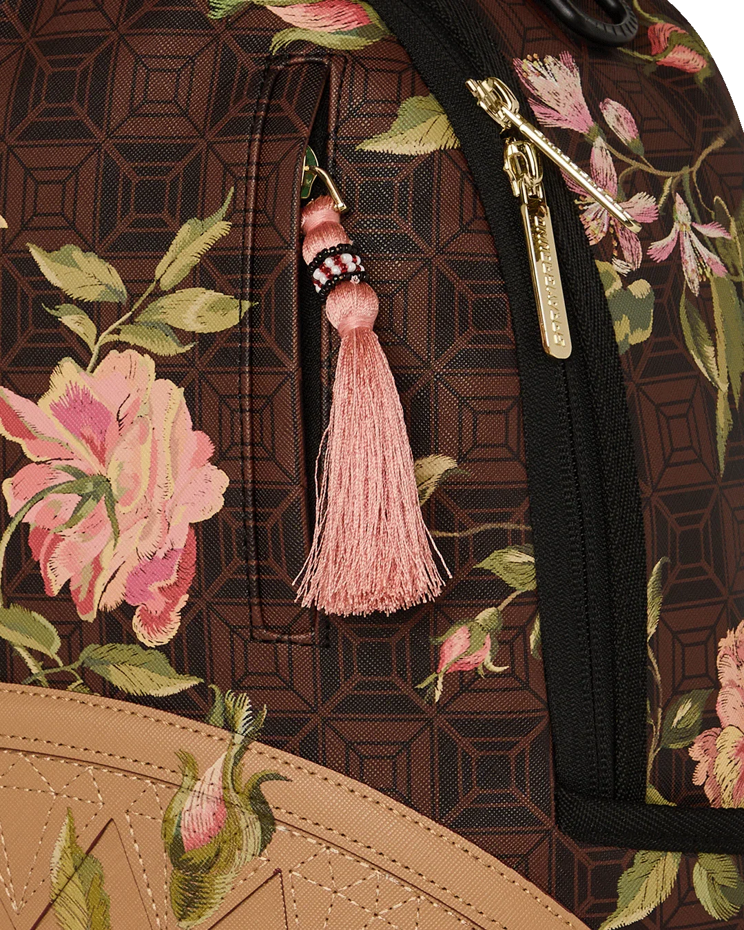 Dettaglio zaino fantasia floreale marrone con zip oro e nappina rosa, accessorio moda uomo donna.