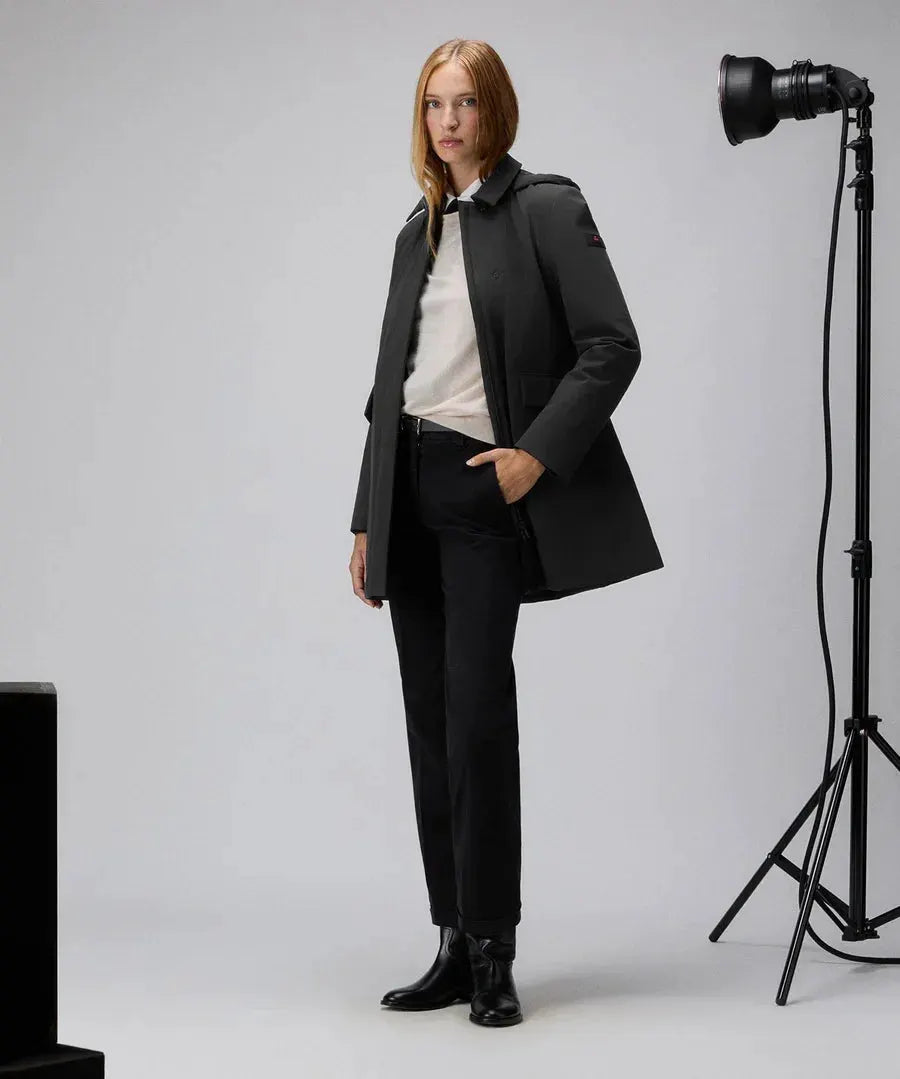 Donna con trench nero slim fit, pantaloni neri e stivaletti, su sfondo studio fotografico