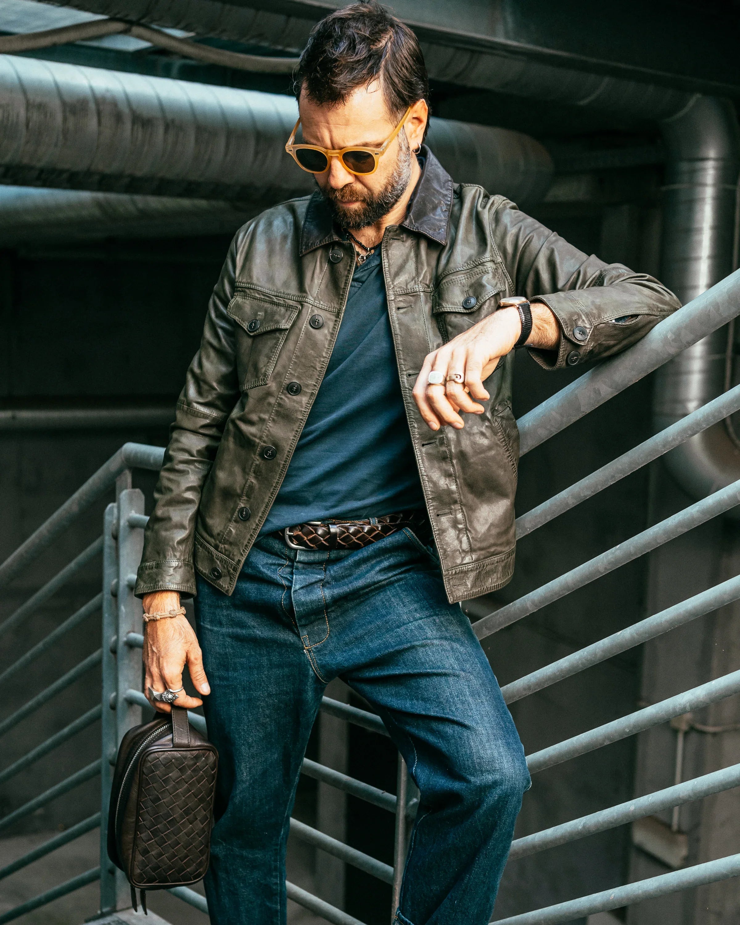 Uomo con giacca di pelle marrone, jeans e borsello, look casual moda uomo.