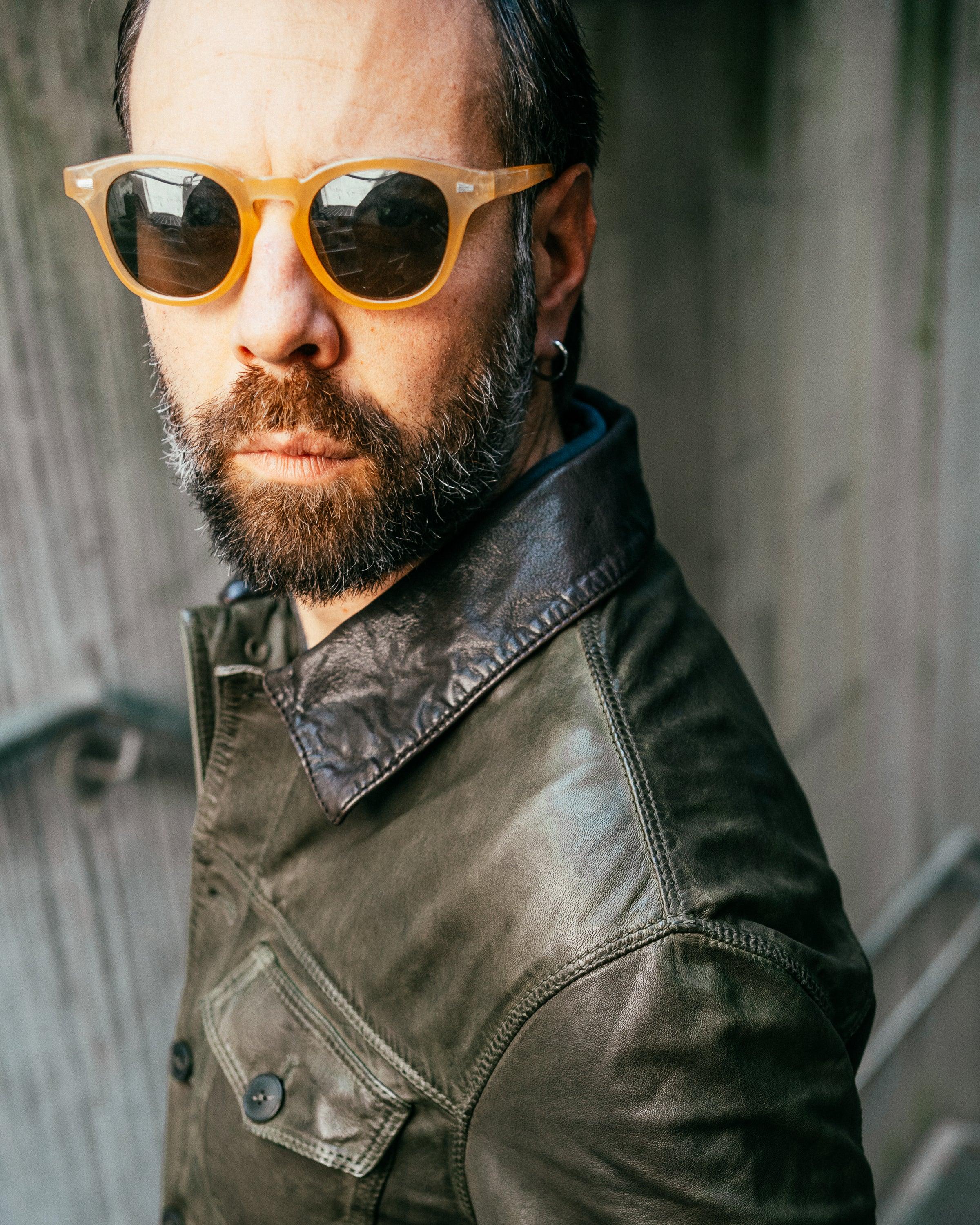 Uomo con giacca di pelle verde scuro e occhiali da sole gialli, moda uomo casual elegante